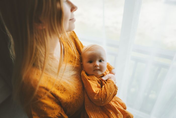 Parent holding a baby by a window.