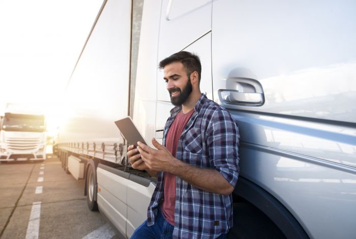 Lorry driver holding a tablet beside his truck.